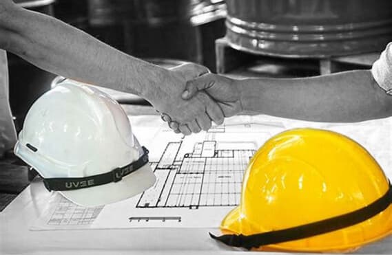 Two hands shaking over a table that has two engineers helmet and a map of a construction site.